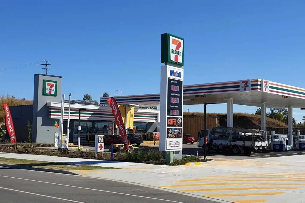 7-Eleven petrol station with orange, red, and green branding and fuel price board