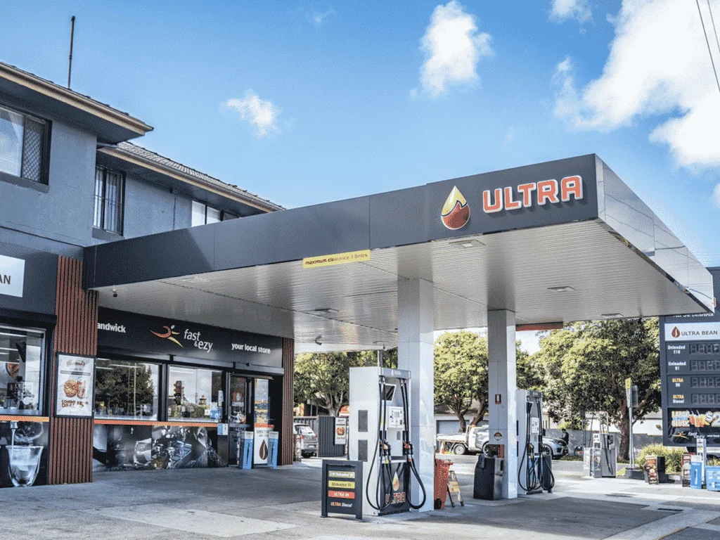 Petrol station forecourt with fuel pumps and price signage in a suburban setting