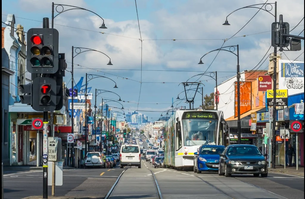 Sydney Road in Coburg with Route 19 tram, shops, and Melbourne CBD skyline in the distance
